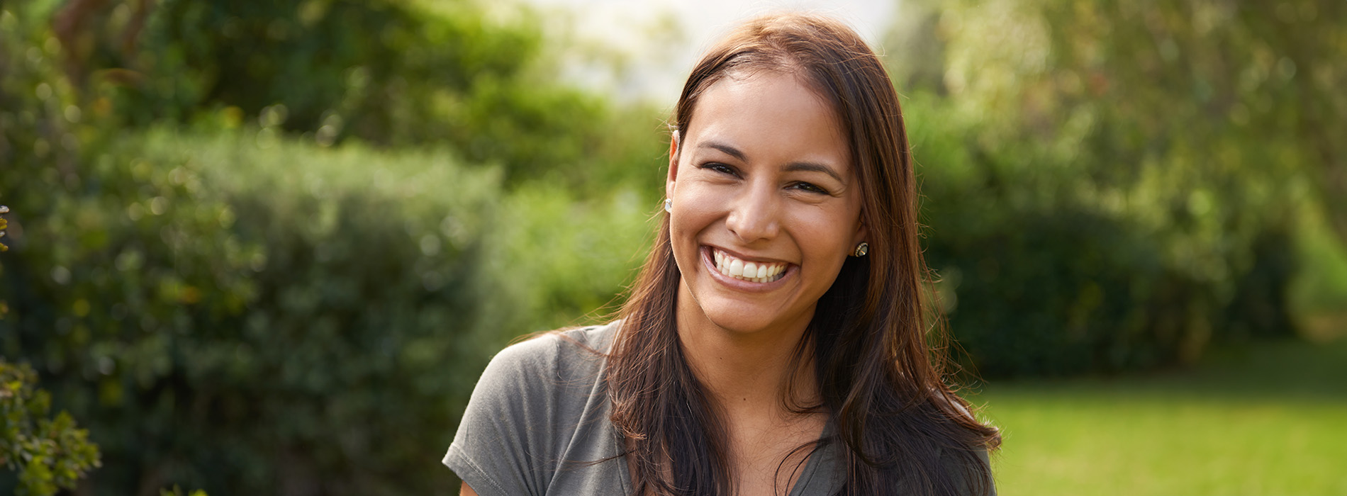 The image is a photograph of a woman with light skin, smiling at the camera. She appears to be in her late twenties or early thirties and has long hair. Her eyes are looking directly at the camera, and she is holding up her index finger near her mouth as if she s making a point or emphasizing something. The background is plain and light-colored, which suggests that this could be a stock photo used for various purposes such as advertising, personal branding, or lifestyle content.
