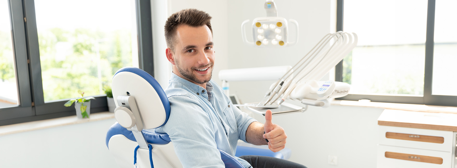 A person is seated in a dental chair, receiving care from a dental professional who stands behind them.