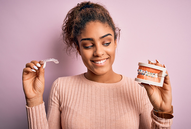 A woman holding a toothbrush and standing next to a product with braces, smiling at the camera.